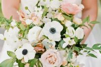 a cheerful spring or summer wedding bouquet of white anemones, blush and pink roses, greenery and blooming branches is ultimate