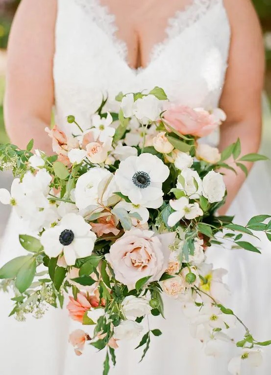 a cheerful spring or summer wedding bouquet of white anemones, blush and pink roses, greenery and blooming branches is ultimate