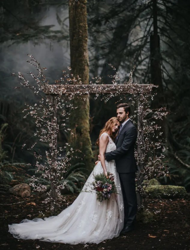 a cherry blossom wedding arch placed in the woods is a creative idea for a moody spring wedding, it will contrast the forest around a lot