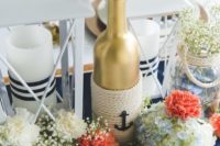 a chic centerpiece with white, coral and blue blooms, a gold bottle with rope, a candle lantern and a jar with baby’s breath
