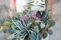a chic dimensional wedding bouquet of greenery, air plants and king proteas plus ribbons is a lovely idea for a boho wedding