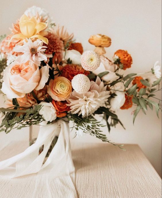 a chic fall wedding bouquet of white dahlias, blush peonies and white and orange peony roses, some white roses, greenery and white ribbons