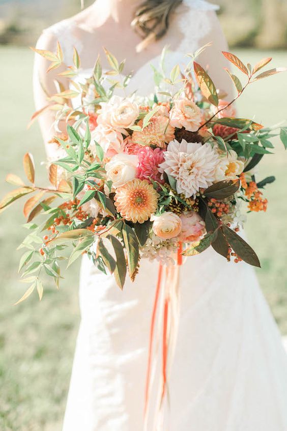 a chic fall wedding bouquet of yellow and pink dahlias, white roses, yellow ranunculus, beerries, greenery and fall leaves