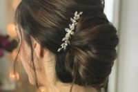 a chic messy French twisted chignon with a volume on top, some locks down and a shiny hairpiece