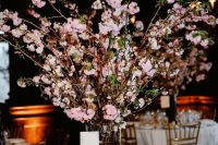 a chic wedding tablescape with neutral linens, tall pink cherry blossom in a vase and gold touches and candles is wow