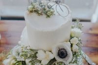 a chic white buttercream wedding cake decorated with white blooms includign anemones and a bike cake topper is wow