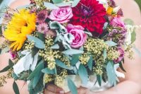 a colorful fall wedding bouquet with pink roses, burgundy dahlias, greenery, dried daisies and sunflowers plus euclayptus