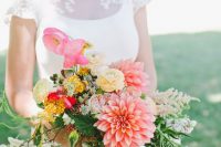 a colorful summer wedding bouquet of pink dahlias, yellow and white ranunculus, berries, greenery, various colorful fillers