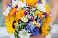 a colorful summer wedding bouquet of white, blue and marigold blooms and sunflowers for a rustic bride