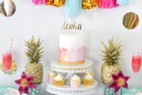 a colorful tropical bridal shower dessert table with a bright tassel garland, gilded pineapples and bright blooms