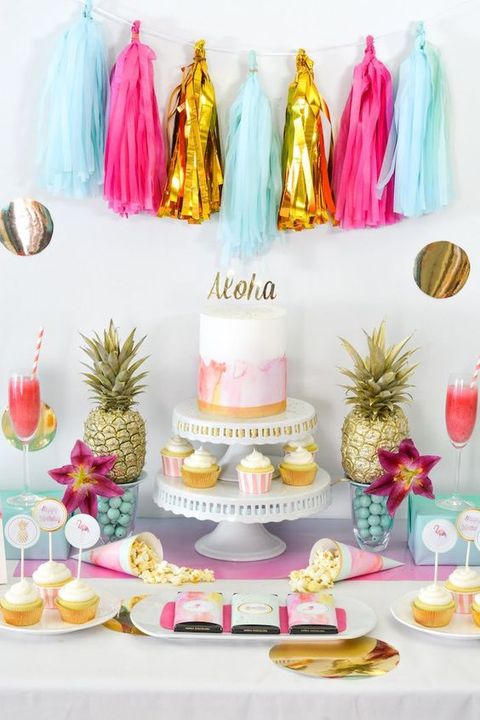 a colorful tropical bridal shower dessert table with a bright tassel garland, gilded pineapples and bright blooms