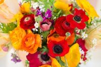 a colorful wedding bouquet of red anemones and ranunculus, yellow poppies and ranunculus, some greenery