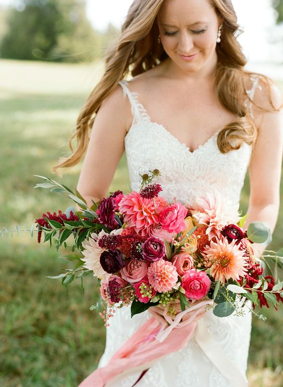 a colorful wedding bouquet with pink and orange dahlias, deep purple and pink ranunculus, greenery and lisianthus plus ribbons
