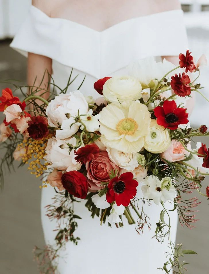 a contrasting wedding bouquet of red anemones, neutral raunuculus, blush peony roses and berries and greenery