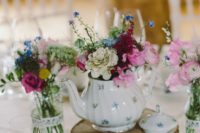 a cool teapot wedding centerpiece of a wood slice, a wood sign, a florla teapot with bright blooms, glasses and bright flowers