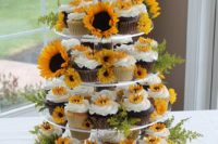 a cupcake stand decorated with fresh sunflowers and cupcakes and the cake themselves decorated with sugar ones, too