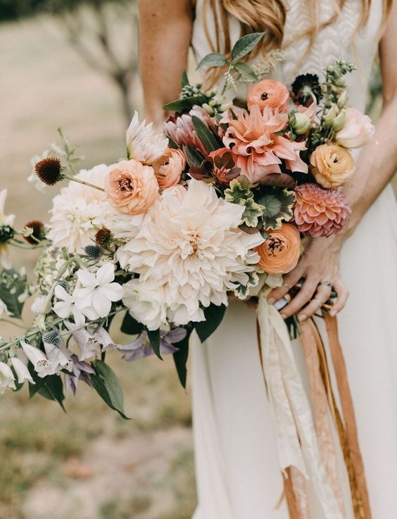 a delicate pastel wedding bouquet of blush and white dahlias, yellow ranunculus, a king protea and some foliage