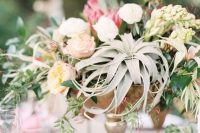 a delicate wedding centerpiece of a tall bowl, neutral and apstel blooms, greenery and an air plant is a lovely idea for spring or summer