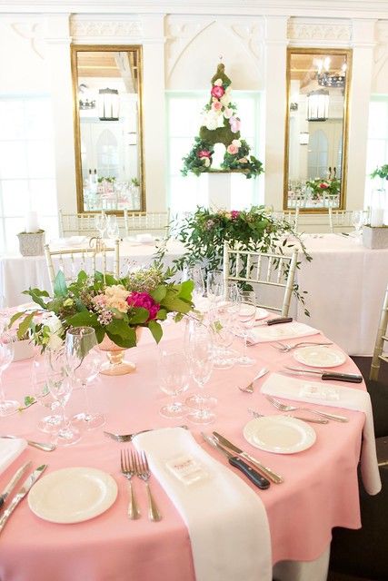 a glam Parisian bridal shower tablescape with a pink tablecloth and neutral napkins, neutral and hot pink blooms and greenery