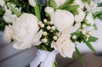 a gorgeous wedding bouquet with white peonies, berries, thistles and greenery plus a white ribbon