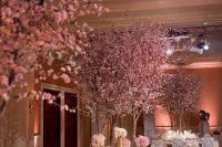 a jaw-dropping formal glam wedding reception space with pink cherry trees in bloom, white flowers in gold vases and pink and purple tablecloths