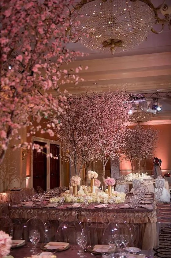 a jaw-dropping formal glam wedding reception space with pink cherry trees in bloom, white flowers in gold vases and pink and purple tablecloths