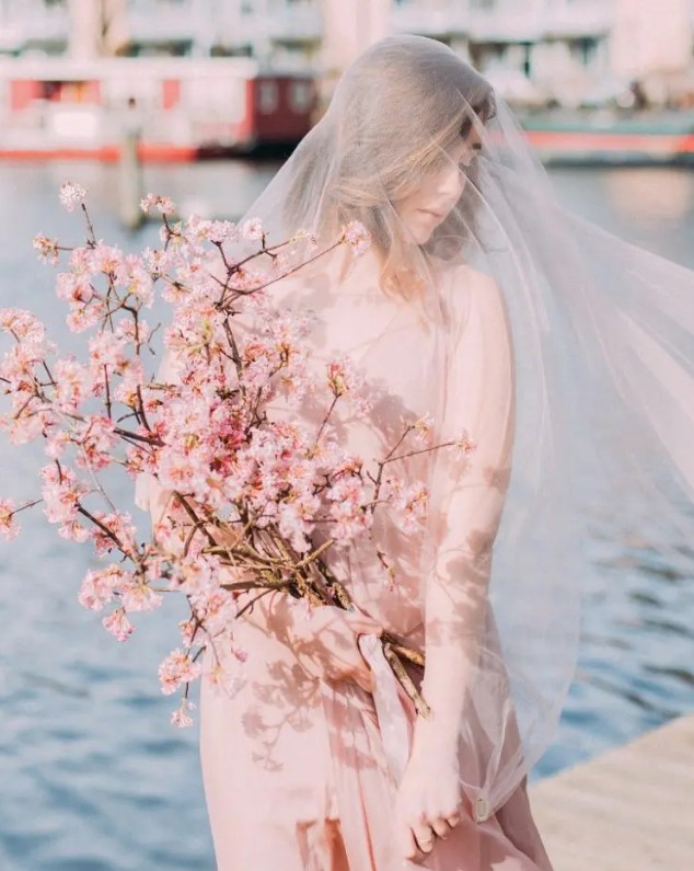 a jaw-dropping spring bridal look with a blush wedding dress and veil paired with a pink cherry blossom wedding bouquet, long stem bouquets are on top