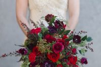 a jewel-tone wedding bouquet of red anemones, burgundy and purple ranunculus and tulipes, greenery and bloomign branches