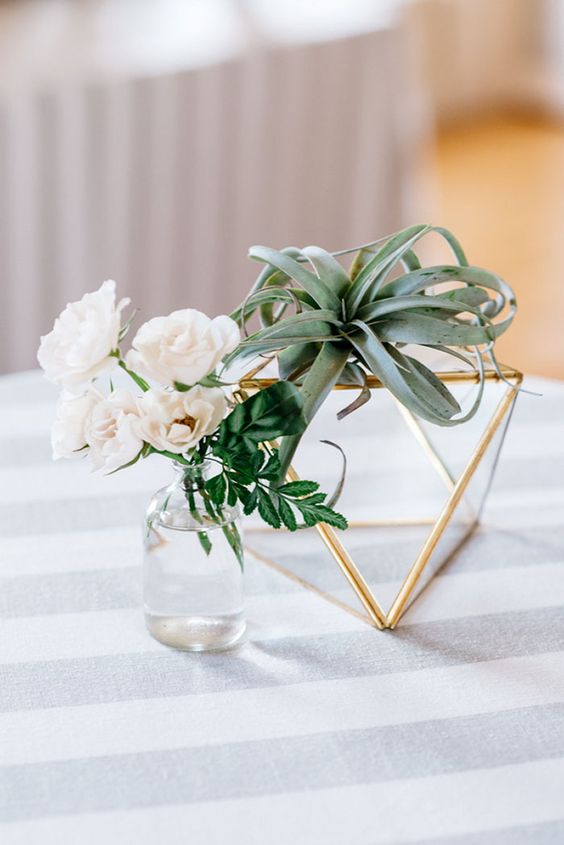 a laconic cluster wedding centerpiece of a faceted terrarium, an air plant, neutral blooms in a bottle is a stylish idea