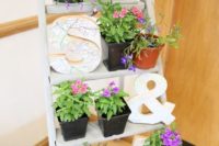 a ladder with potted greenery and bright flowers plus letters is a cool idea to decorate your space in a bold way