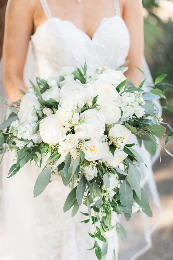 a large and lush wedding bouquet with white peonies and other blooms and much greenery, which is cascading