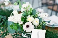 a lovely and fresh wedding centerpiece with white hydrangeas, anemones and ranunculus, greenery and an additional greenery table runner