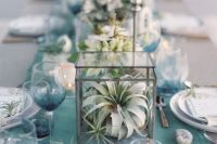 a lovely coastal wedding tablescape with a blue table runner, white blooms and air plants in terrariums plus candles around