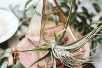 a lovely wedding centerpiece of a wood slice, greenery, a candle lantern with an air plant is a stylish idea for a wedding