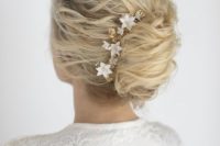 a messy and wavy French twist updo with a messy top and chingon plus a gold and white floral hairpiece