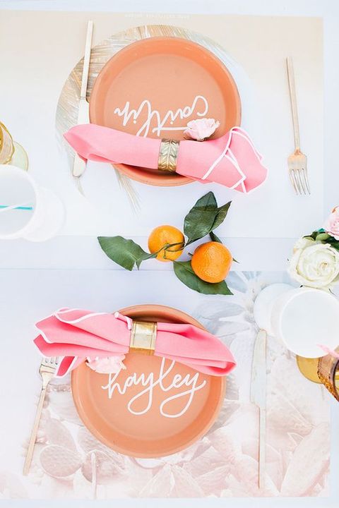 a modern tropical bridal shower tablescape with peachy chargers, pink napkins with gold rings, gold cutlery and citrus
