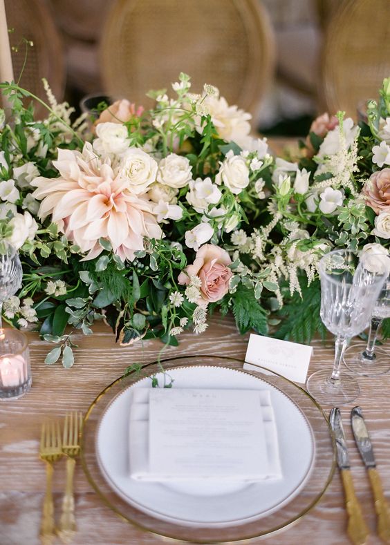 a neutral wedding centerpiece of greenery, white garden roses, blush dahlias and roses and some neutral fillers