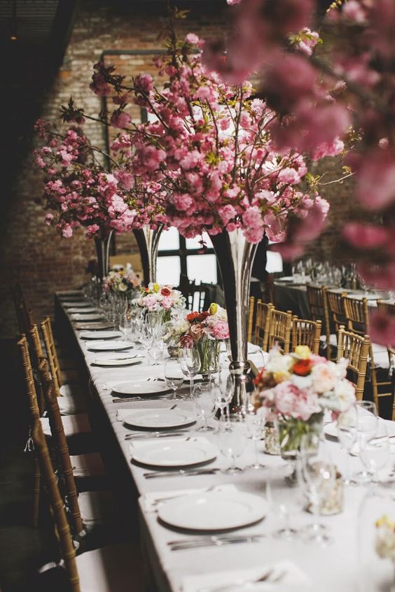 a neutral wedding tablescape with a neutral tablecloth, white plates, tall pink cherry blossom and candles is a lovely idea for spring