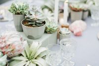 a neutral wedding tablescape with potted succulents, an air plant and king proteas, candles and a grey tablecloth