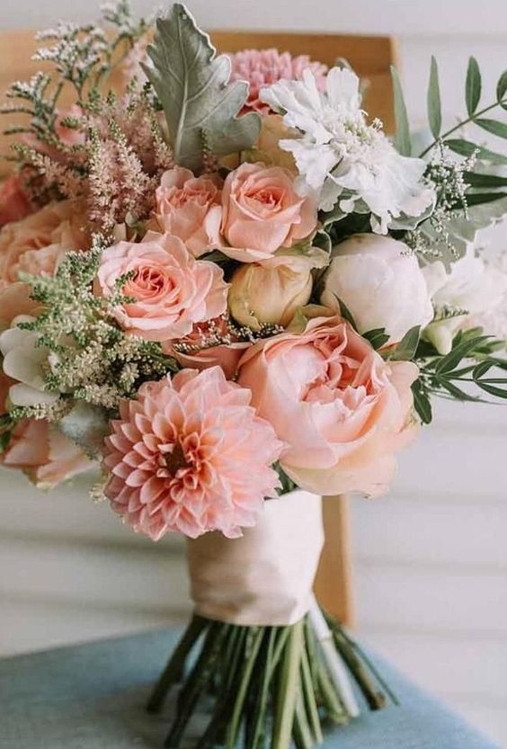 a pastel wedding bouquet of blush roses and dahlias, white peonies, greenery, white and pink astilbe and a neutral wrap