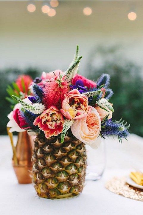 a pineapple centerpiece with a bright floral arrangement and touches of greenery for a tropical bridal shower