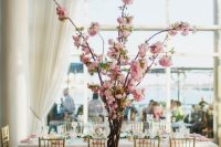 a pretty spring wedding tablescape with pink cherry blossom as a centerpiece, pink napkins and blooms and amber glasses