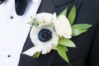 a pretty wedding boutonniere of white roses and an anemone, some greenery and berries is a chic idea for spring or summer