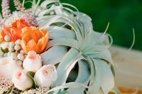 a pretty wedding centerpiece of blush and orange blooms, berries and large air plants is a very unusual solution