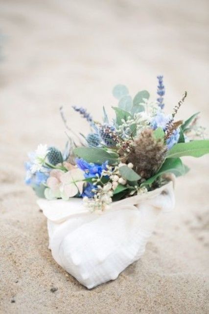 a seashell decoration with fresh blue blooms, greenery and thistles is a cute idea of a bridal shower centerpiece