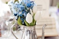 a silver teapot with white tulips and blue hydrangeas for a simple and chic wedding centerpiece