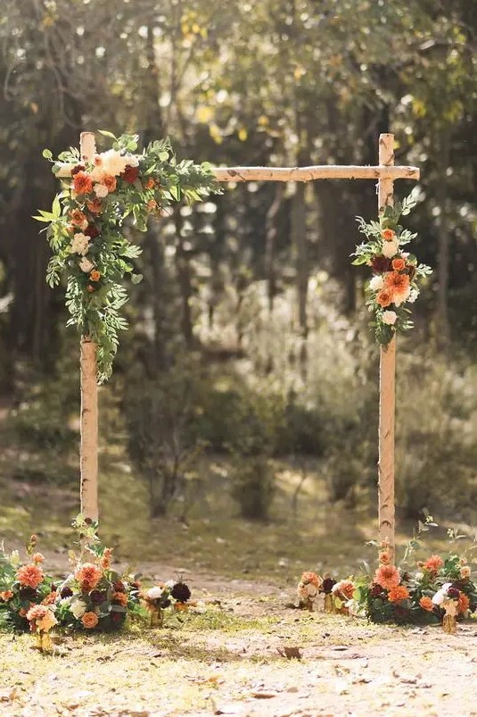 a simple and stylish rustic wedding arch of branches, greenery, white, rust and burgundy dahlias and deep purple touches
