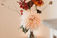 a simple fall wedding centerpiece of a blush dahlia, some bold fall blooms, a mini pumpkin, apple and a pinecone