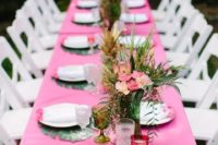a simple tropical shower tablescape with a pink tablecloth, bright floral arrangements and tropical leaf placemats