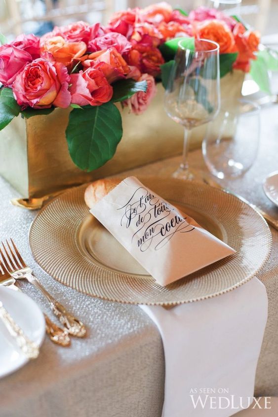 a sophisticated Parisian themed bridal shower table with bright pink blooms in a gold box, gold chargers and cutlery